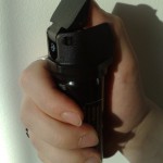 A woman holding a black canister of pepper spray